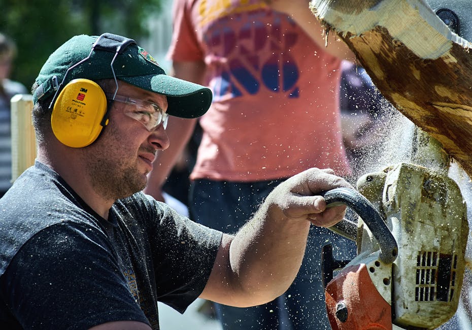 A man wearing safety gear operates a chainsaw outdoors, showcasing woodworking and safety practices.