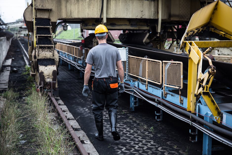A worker in safety gear examines industrial machinery in an outdoor setting, showcasing industry work.