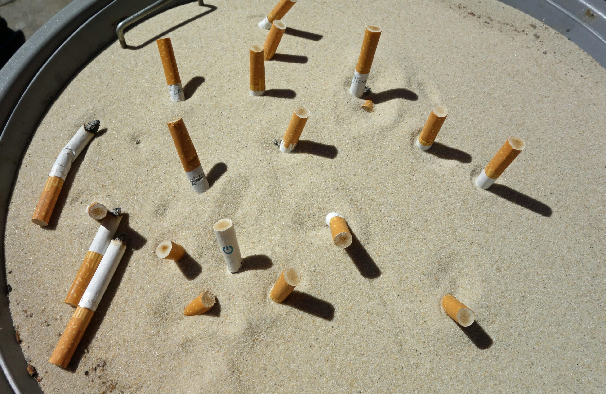 Image showing multiple cigarette butts discarded in a sand-filled ashtray, highlighting littering.