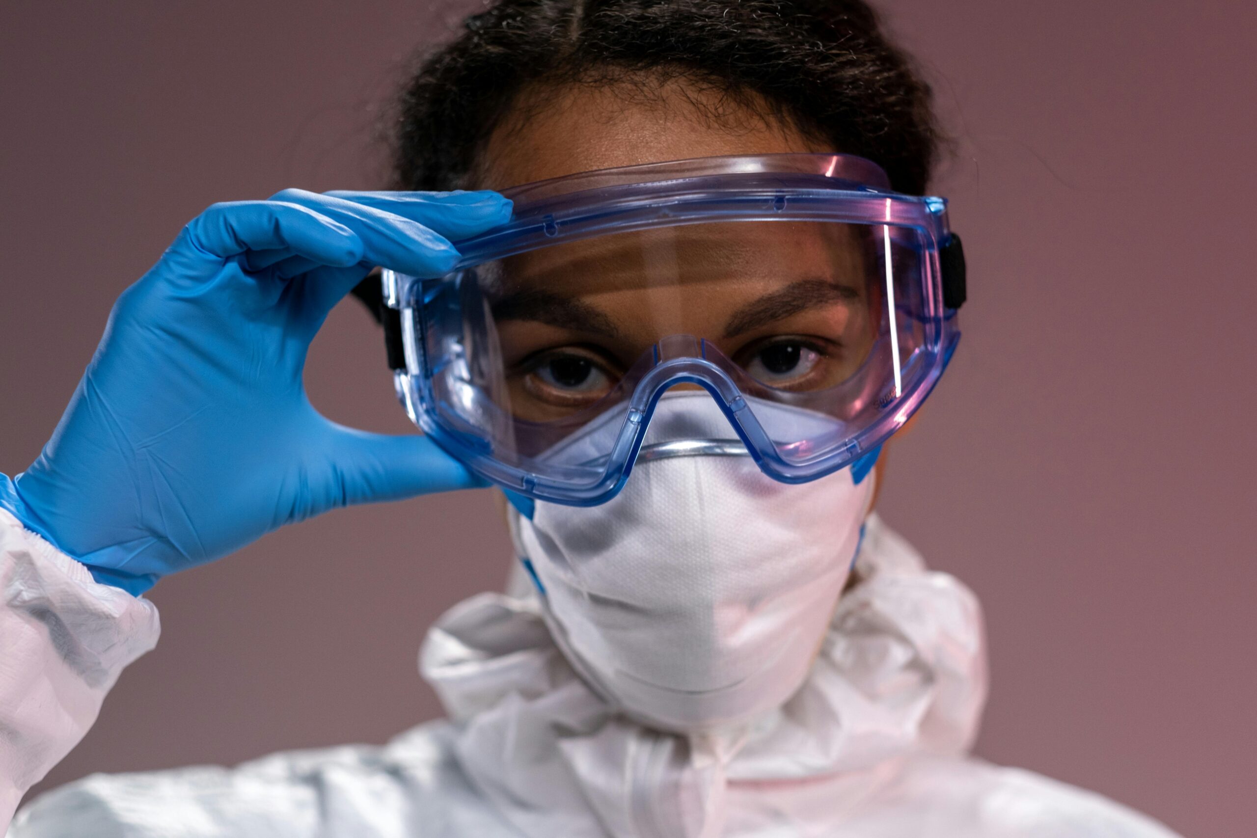 Close-up portrait of a healthcare worker wearing full protective equipment, eyeglasses, mask, and gloves.